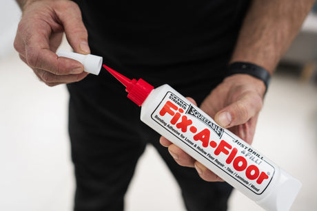 Person holding a squeezable tube of Fix-A-Floor Extra Strength Bonding Adhesive, opening the red nozzle cap to apply the loose and hollow floor tile repair adhesive