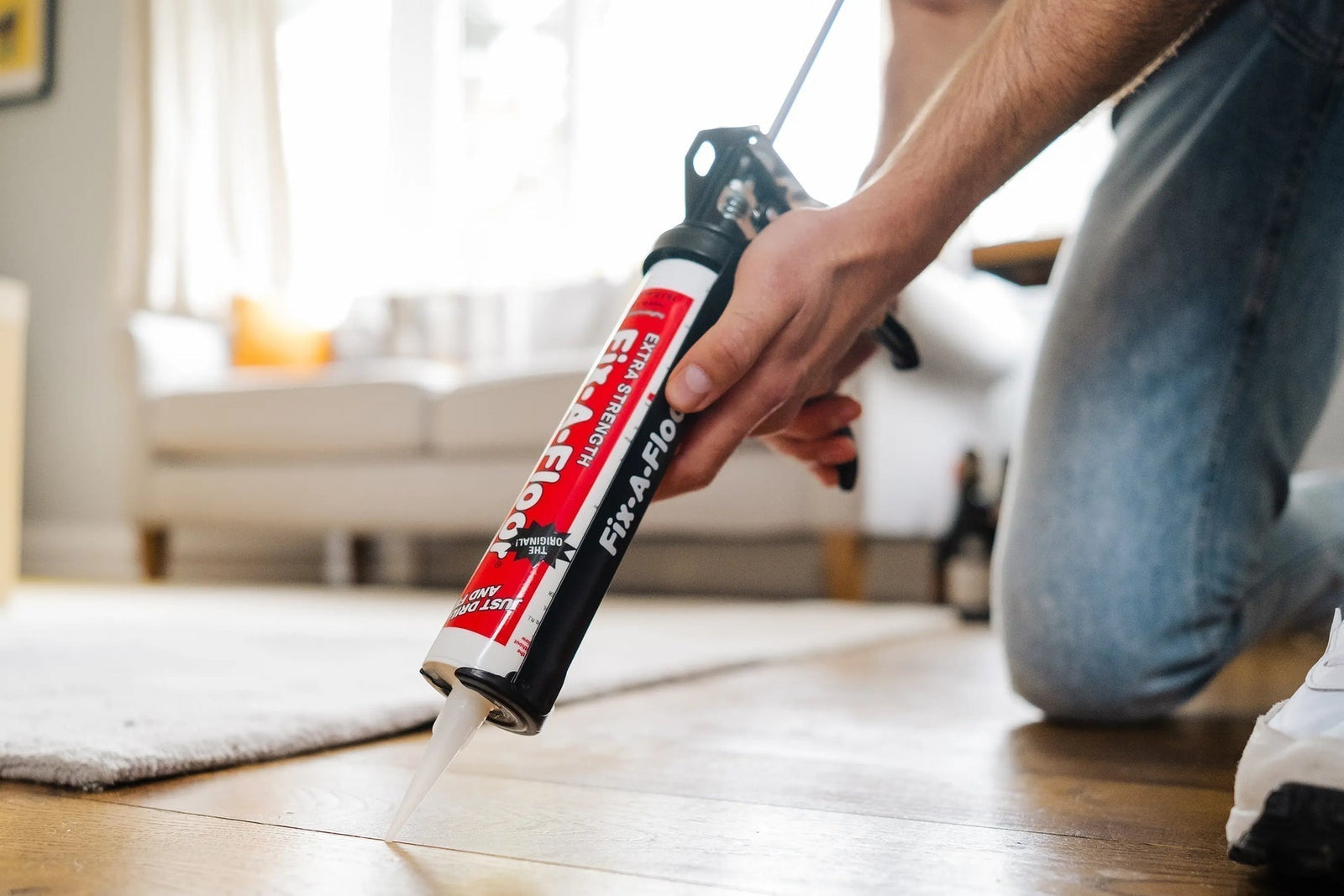 Person applying Fix-A-Floor extra strength bonding adhesive into a gap between wooden floorboards using a caulking gun