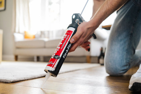Person applying Fix-A-Floor extra strength bonding adhesive into a gap between wooden floorboards using a caulking gun