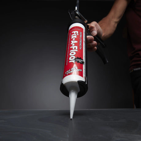 Close-up of a person applying Fix-A-Floor Extra Strength Adhesive with a caulking gun into a floor crack or grout line.