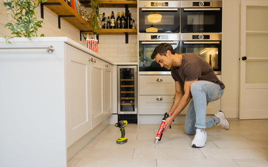 Man fixing squeaky floor with fix a floor adhesive and applying it via caulking gun